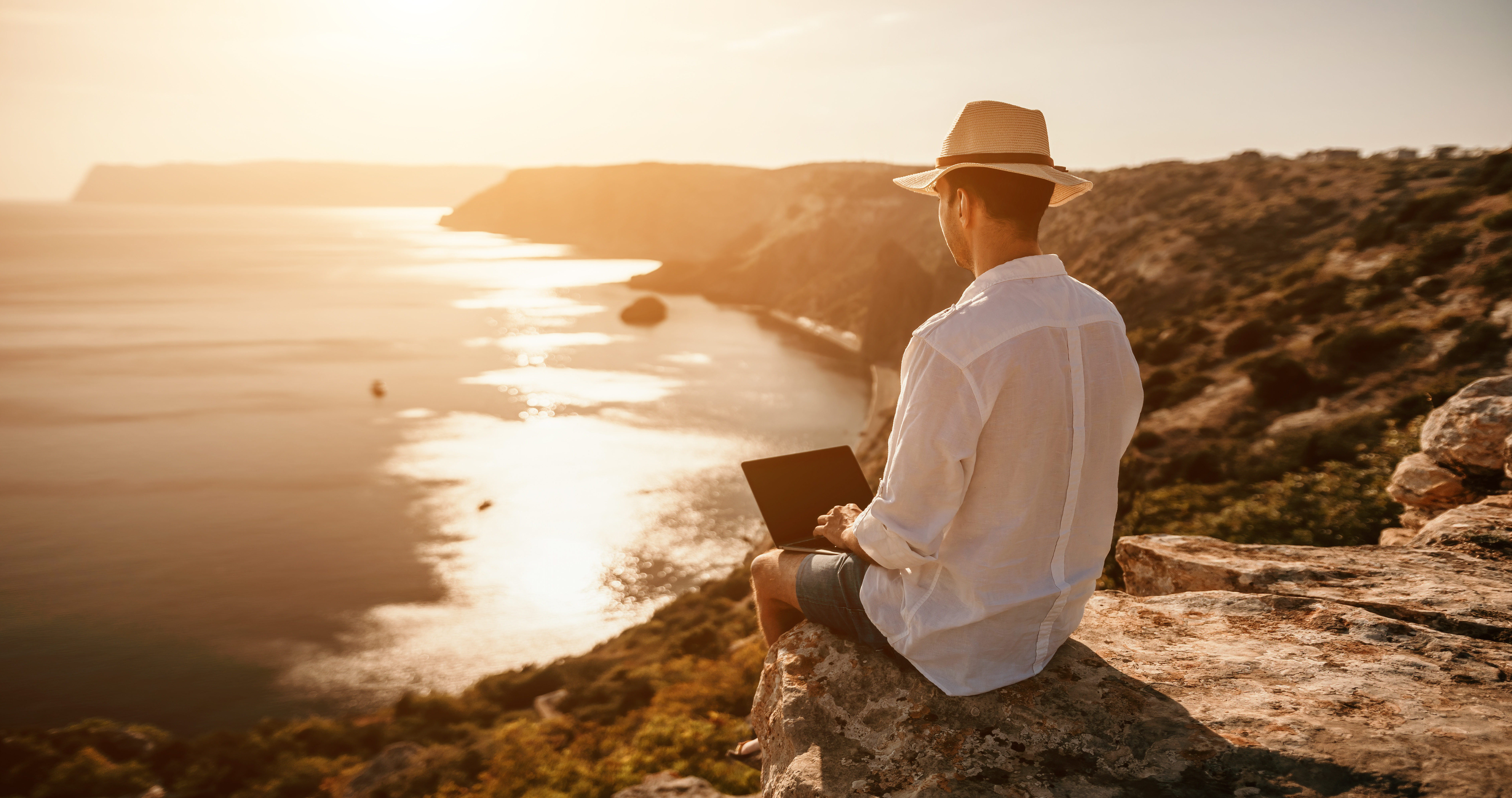 man sitting near beach working on laptop